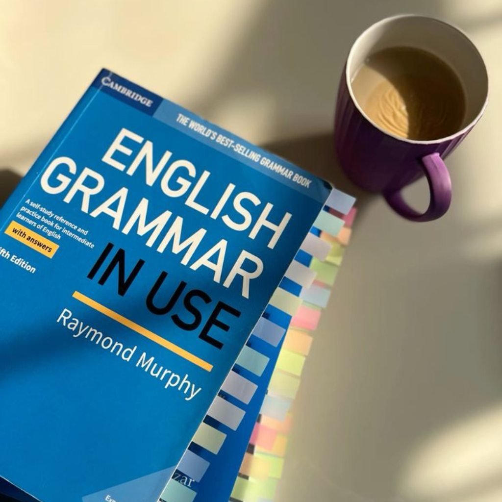 "English Grammar in Use by Raymond Murphy alongside a cup of coffee, representing self-study, English grammar learning, and basic English speaking course preparation."